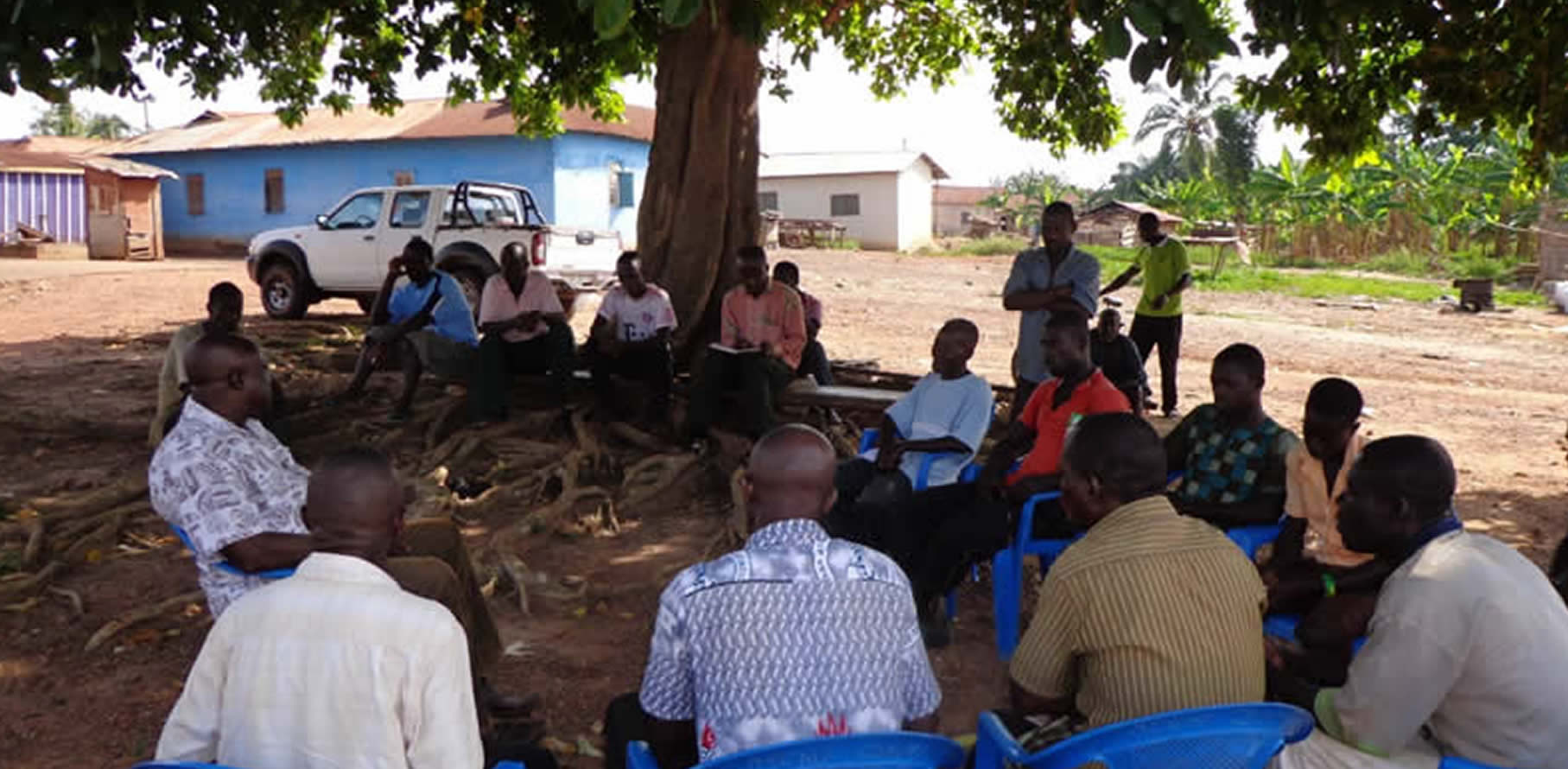 Community discussion meeting held outdoors under a tree in Ghana